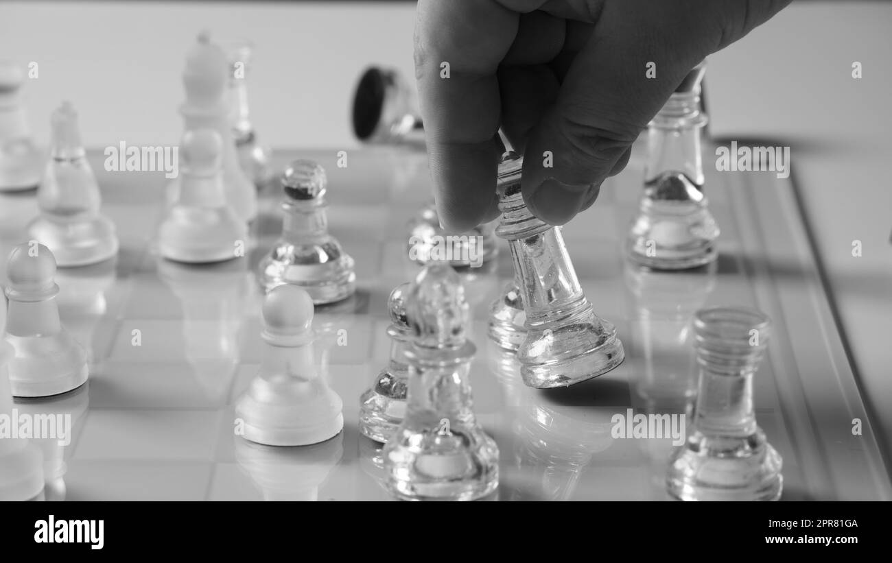 A chessboard with a hand starting to move a chess piece. Clear glass chess figures on a chessboard Stock Photo
