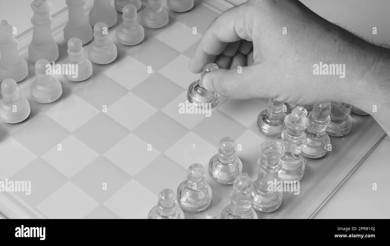 A chessboard with a hand starting to move a chess piece. Clear glass chess figures on a chessboard Stock Photo