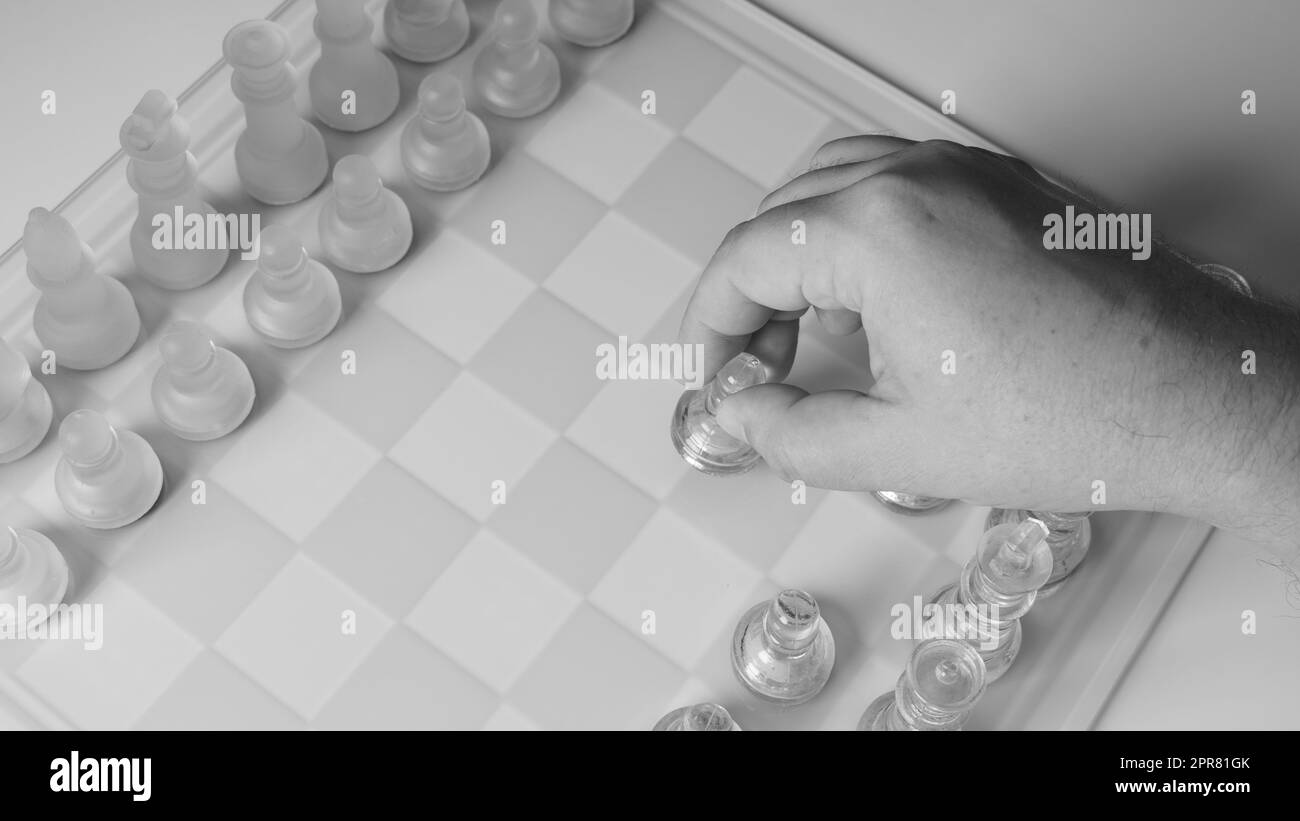 A chessboard with a hand starting to move a chess piece. Clear glass chess figures on a chessboard Stock Photo