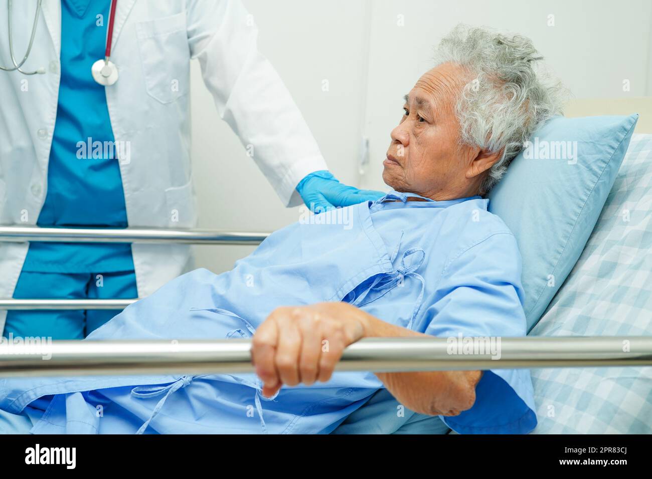 Asian elder senior woman patient holding bed rail while lie down with hope waiting her family in hospital. Stock Photo