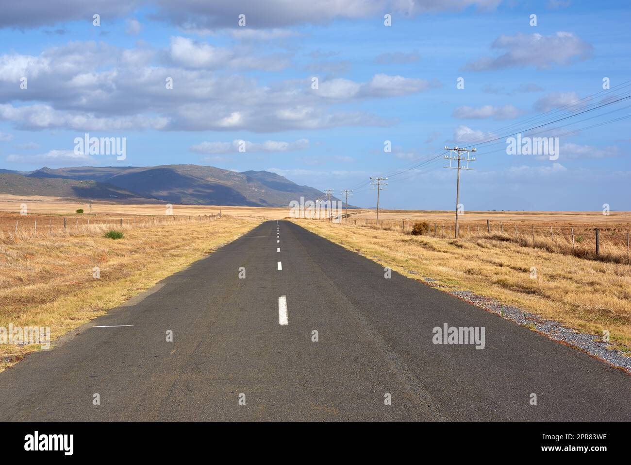 Landscape of tar road leading past freshly harvested farm in Western Cape, South Africa. Blue sky, scenic rural countryside street of ploughed agricultural field. Travel to sustainable grain pasture Stock Photo