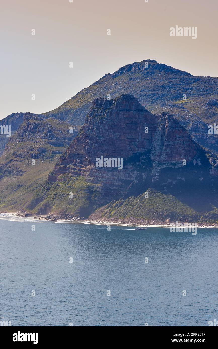 A mountain in the ocean at Hout Bay, South Africa on a summer day. Sea tropical landscape or Mediterranean seascape on a hot afternoon. Wild coast beach scenic view as holiday or vacation destination Stock Photo