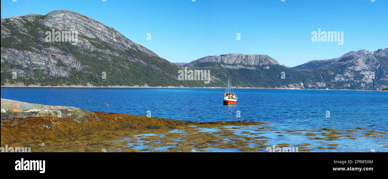 Wide angle landscape of a remote fishing lake near mountains. Stone hills by the nordic seaside with a bright blue sky. Calm water for a peaceful environment on a holiday in scenic Nordland nature Stock Photo