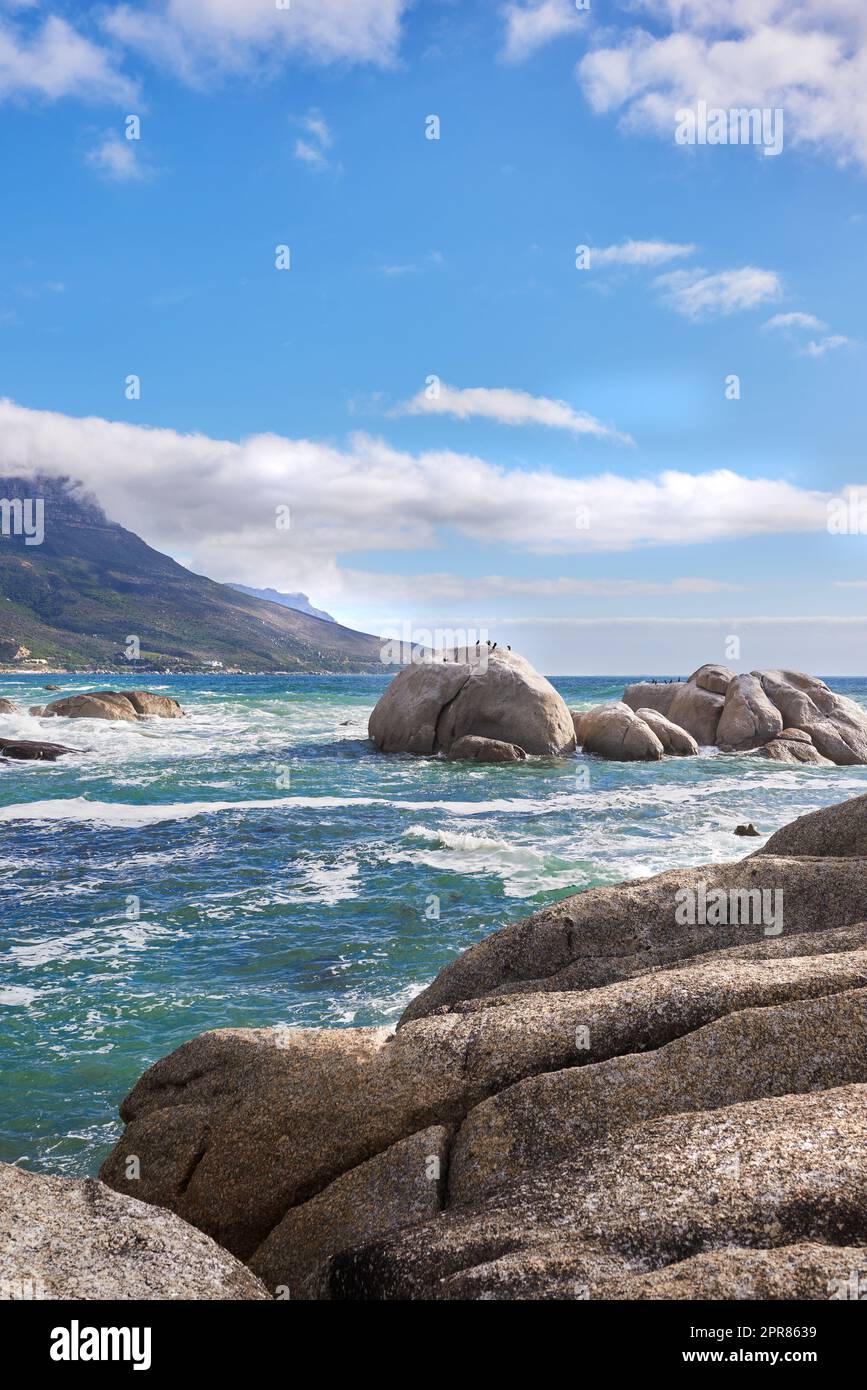 Landscape view of sea water, rocks and a blue sky with copy space in Camps Bay Beach, Cape Town, South Africa. Calm, serene, tranquil, ocean and relaxing nature scenery. Waves washing on rocky shore Stock Photo