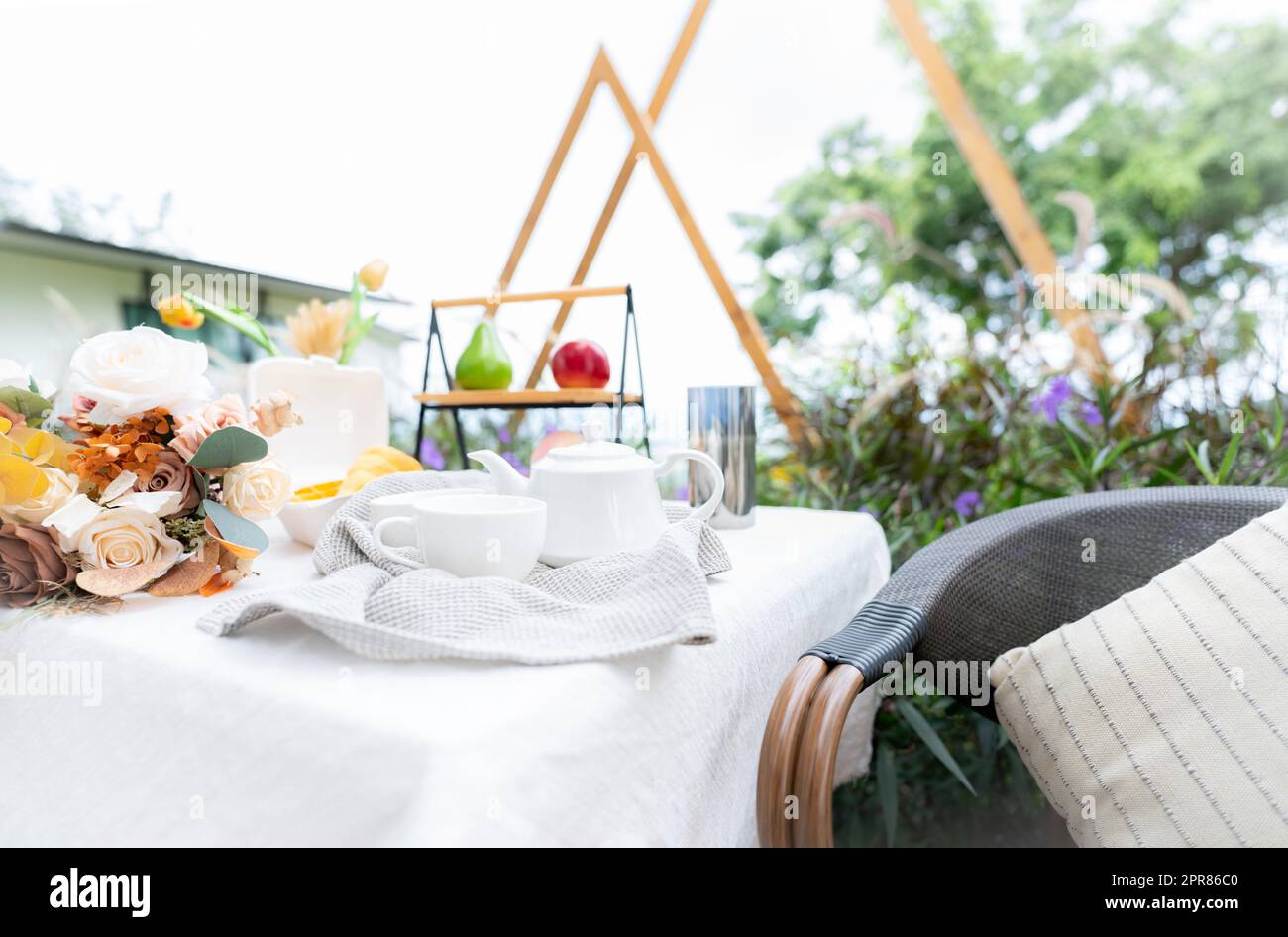 Coffee cup and flowers bouquet on table in garden. Afternoon tea concept. Home outdoor furniture. Wicker chair and table with white tablecloth in vintage style. Cozy chair and table on the terrace. Stock Photo