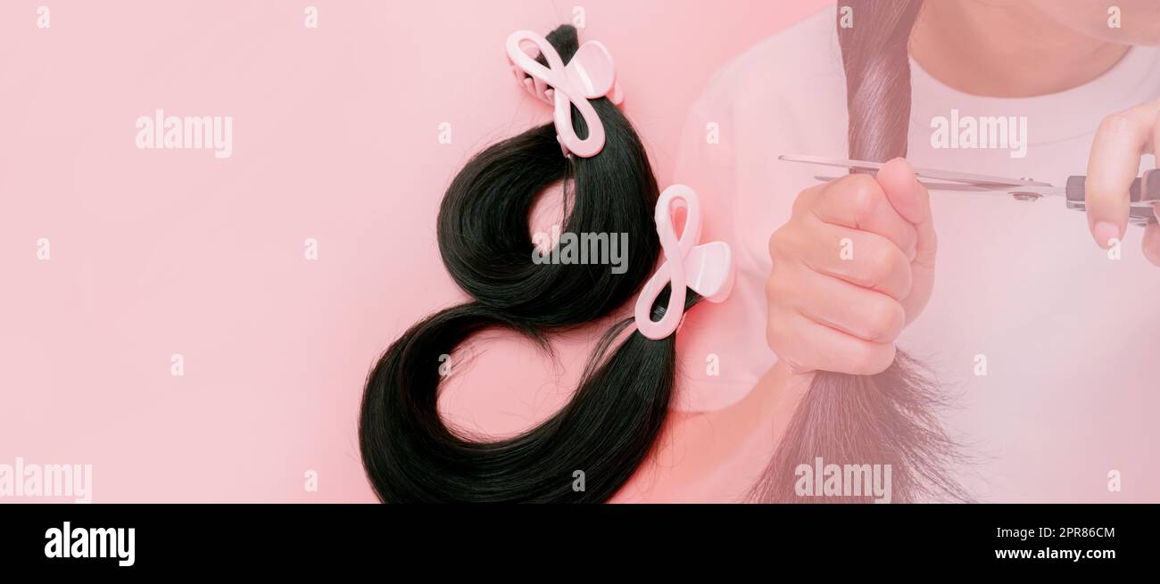 Hair donation for breast cancer person concept. Donate hair to wigs for breast cancer patients. Donate to cancer charity. Asian woman cutting long hair with scissors for donating on pink background. Stock Photo