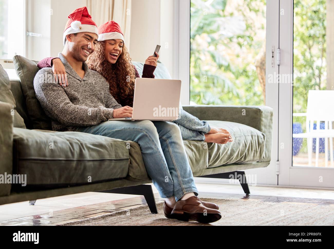 Were doing all our Christmas shopping online. Shot of a young couple doing online shopping while wearing Christmas hats at home. Stock Photo