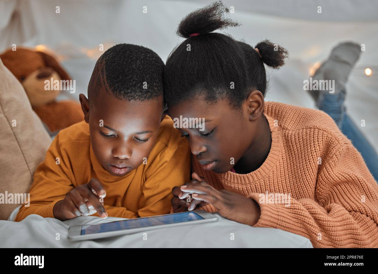 We can play this game together. a brother and sister using a digital tablet together at home. Stock Photo