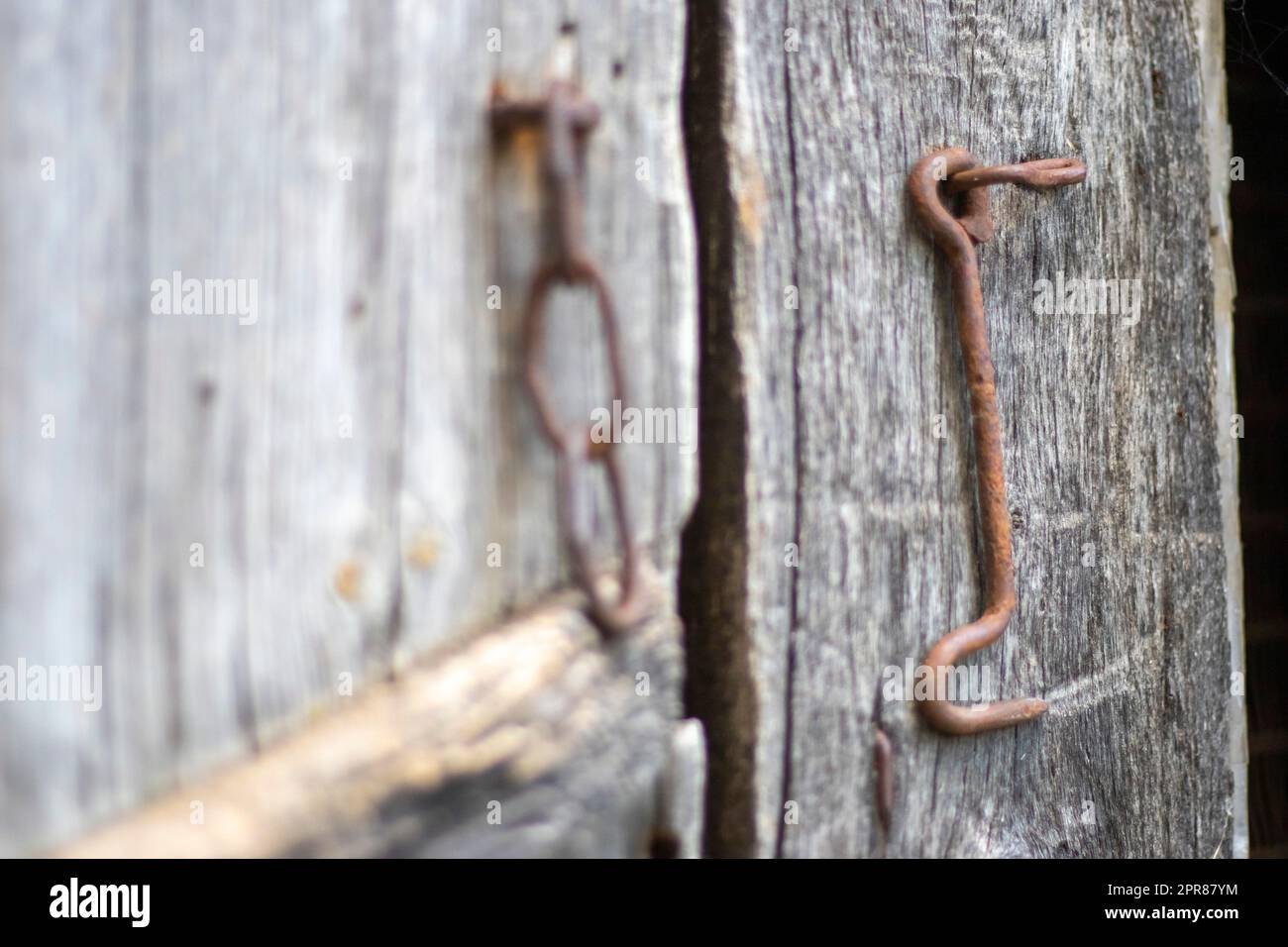 Isolated old rusty door latch on a wooden door. Close-up. Problematic weathered panels. Old wall texture background. Detail of an old wooden door with a rusty door latch. Stock Photo