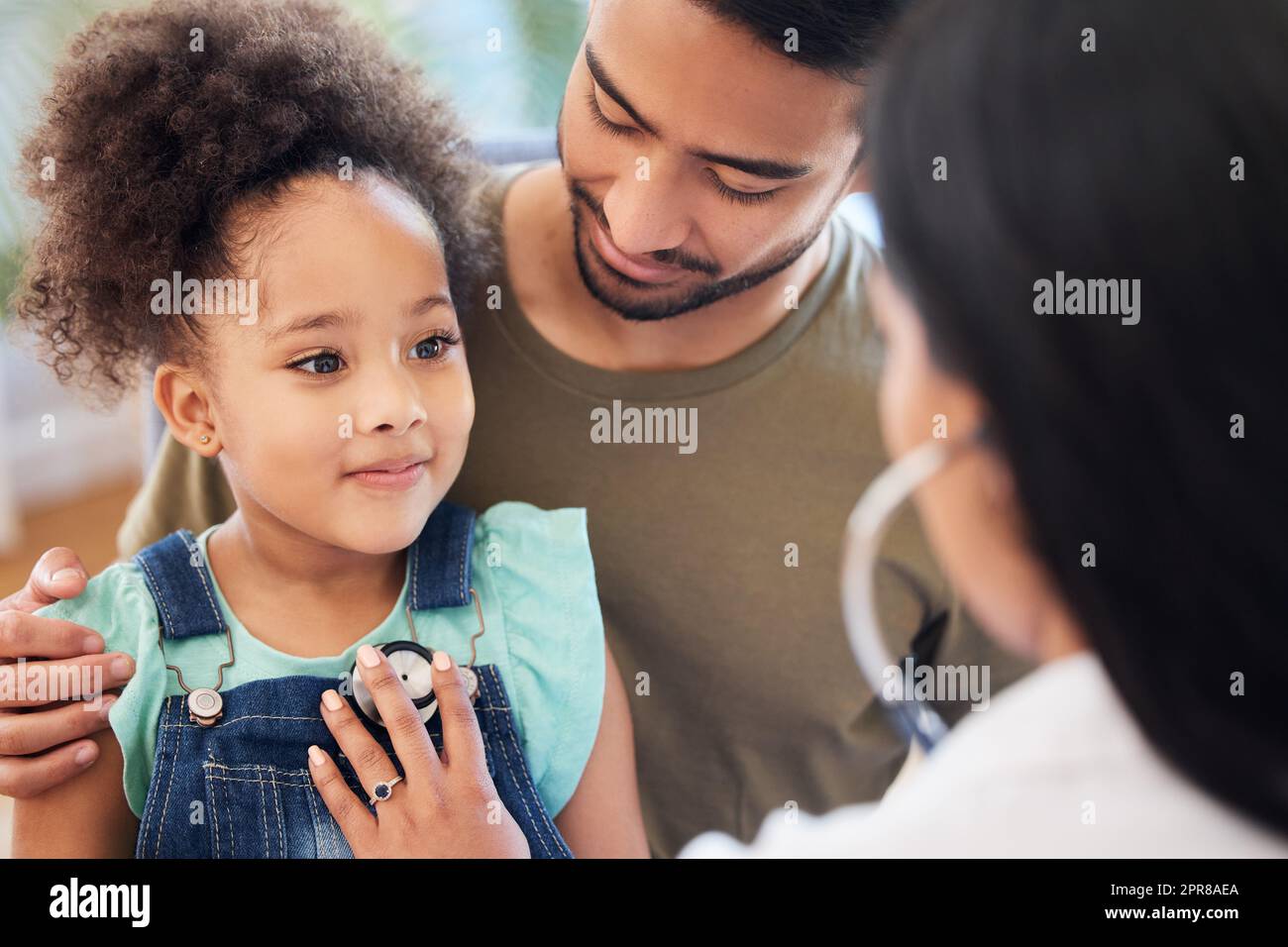 My doctor is really nice. Shot of a little girl sitting on her fathers lap while being examined by her doctor. Stock Photo