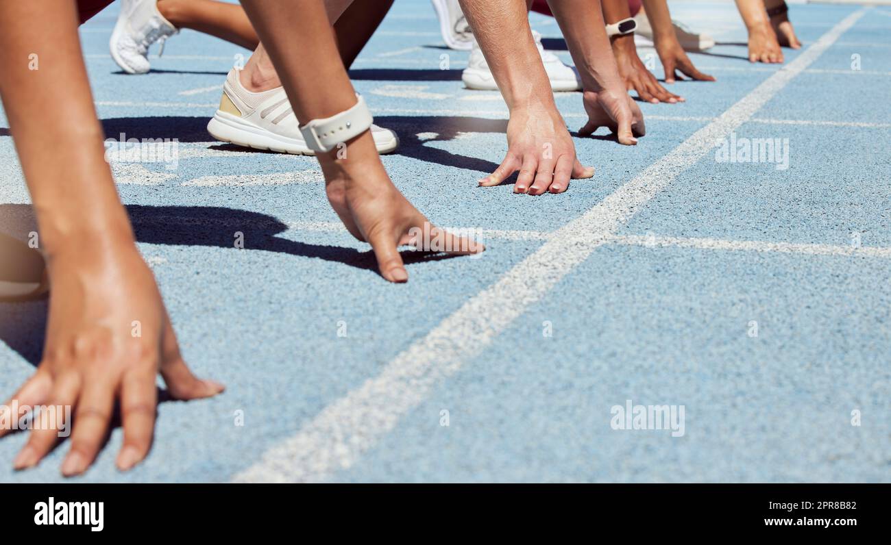 Closeup of determined group of athletes in starting position line to begin sprint or run race on sports track stadium. Hands of diverse sports people ready to compete in track and field olympic event Stock Photo