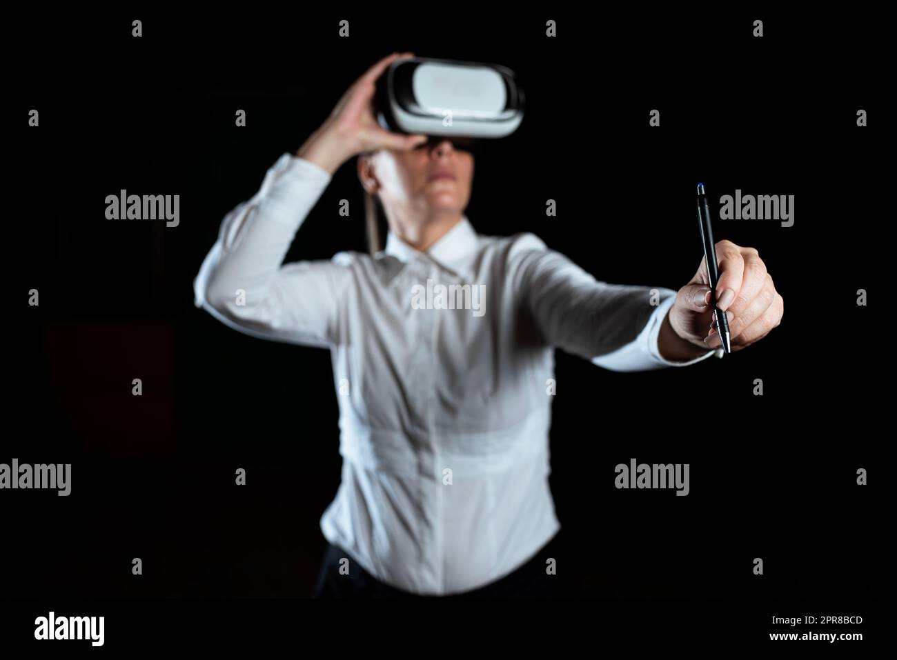 Businesswoman Wearing Virtual Reality Simulator And Holding Pen. Woman Wearing Vr Headset While Attending Professional Training Through Modern Technology. Stock Photo