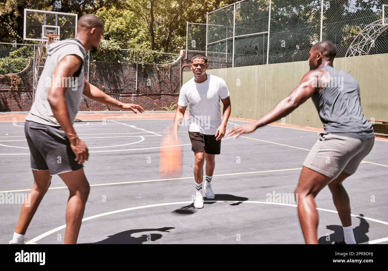 Three african american men playing basketball on a court outdoors. Black man and his sporty friends being athletic outside. Group of basketball players competing in a match or game for recreation fun Stock Photo
