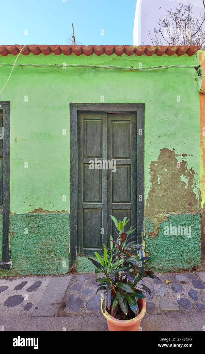 Old abandoned house or home with a weathered green wall and aging wooden door. Vintage and aged residential building built in a traditional architectural style or design with a cobble stone road Stock Photo