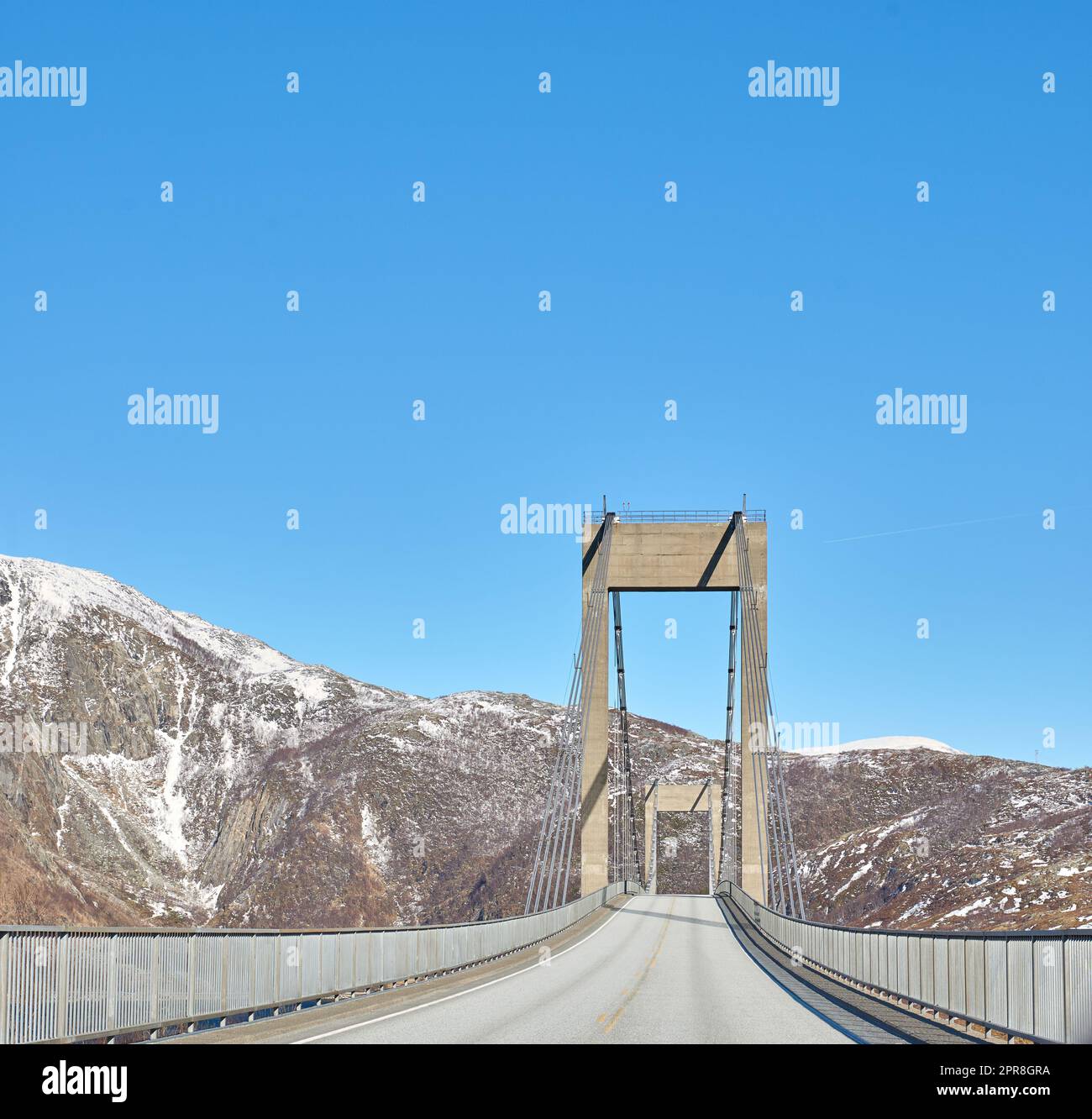 Empty road in the mountains against a blue sky with copy space. Deserted highway crossing in the cold snowy and grey hills around Bodo in Norway. Polar landscape of old bridge over a ravine or river Stock Photo