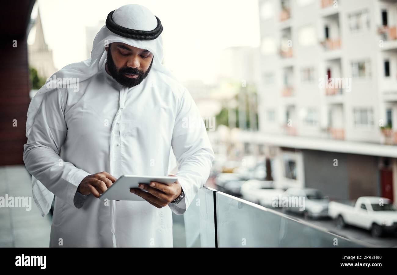 He does some of his best work out here. a businessman dressed in traditional Islamic clothing working on his office balcony. Stock Photo