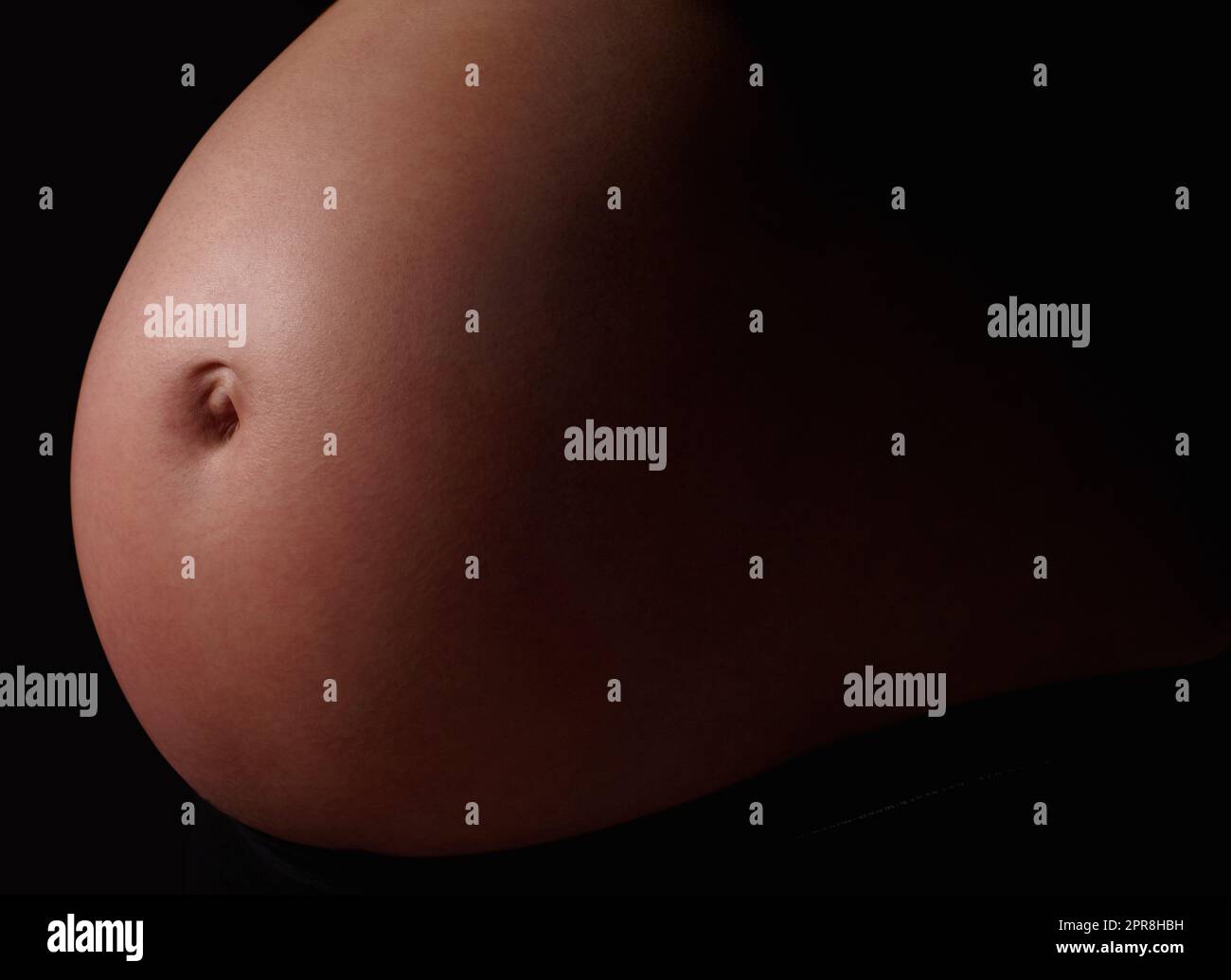 Detail shot of a pregnant womans belly against black. Belly of a pregnant woman against black background. Stock Photo