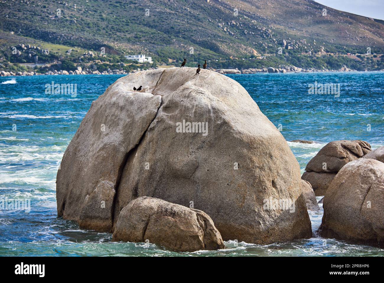 Big rocks in the blue ocean with mountains in the background. Stunning nature landscape or seascape on a summer day. Boulders or large natural stones in aqua sea water with beautiful rough textures Stock Photo
