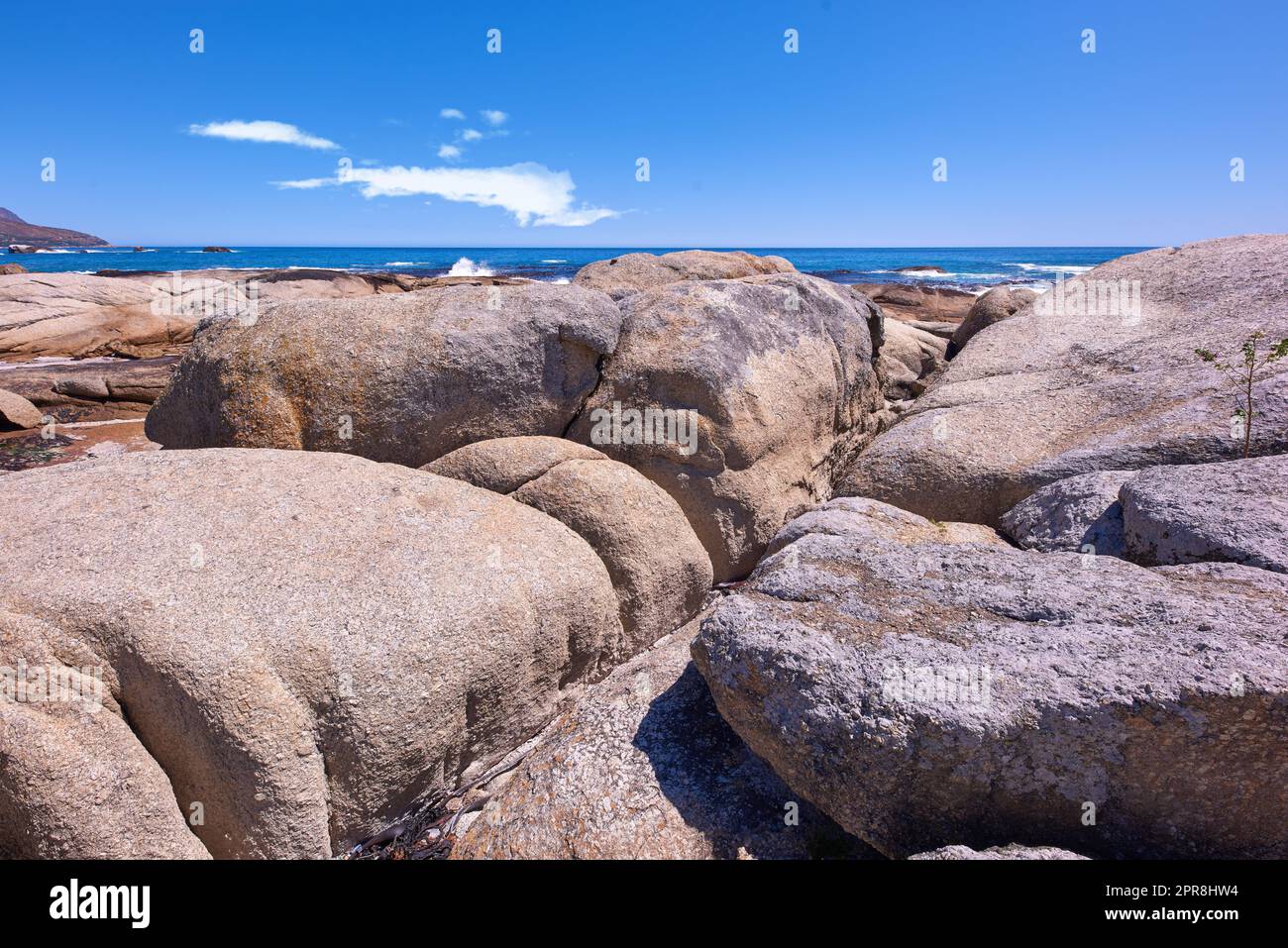 Rocky coastline with the ocean and blue sky with copyspcae in the background. Stunning nature landscape or seascape of rocks. Boulders or big natural stones in the sea with beautiful rough textures Stock Photo
