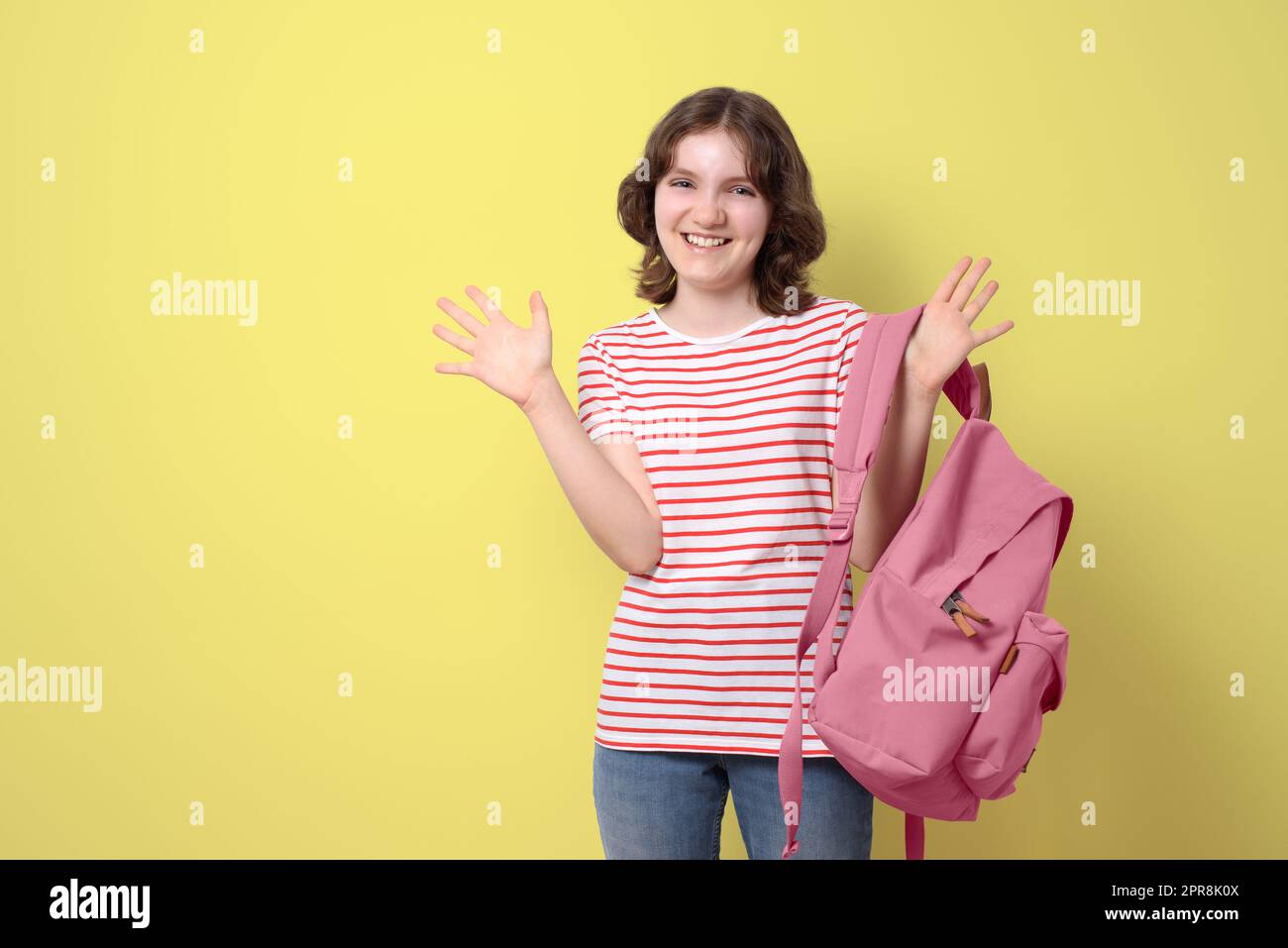 Happy schoolgirl smiling and holding backpack, looking at camera, on yellow background Stock Photo