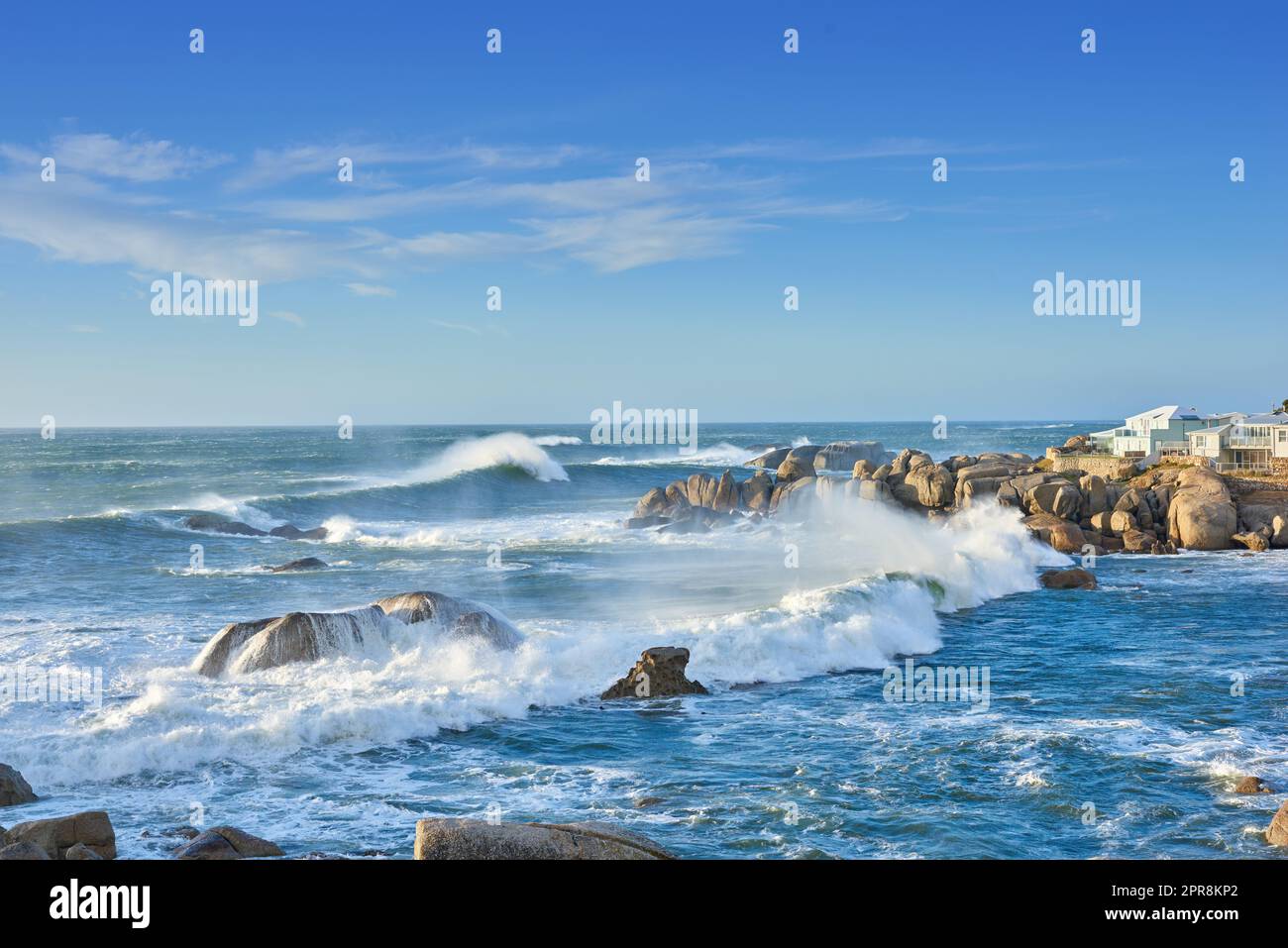 A rocky coastline in the Cape Province, South Africa. Ocean waves crashing on coastal rocks on a sunny summer day with blue clear skies and a scenic tropical landscape beachfront in the Western Cape Stock Photo