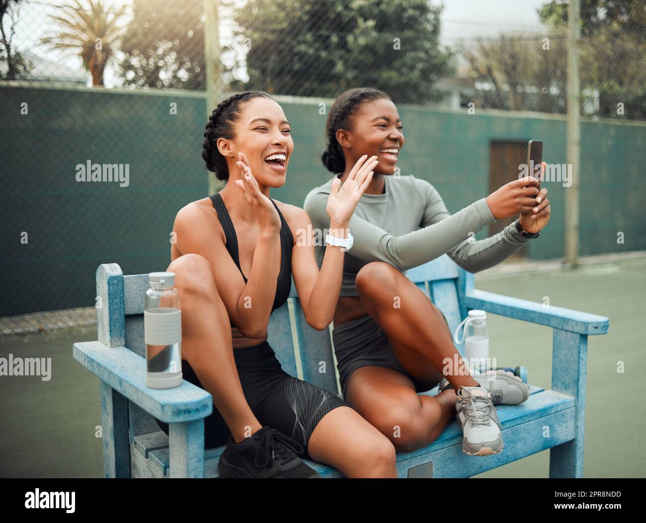 Cheering on their teammates. two attractive young female athletes sitting on a bench at a sports court watching a competition. Stock Photo