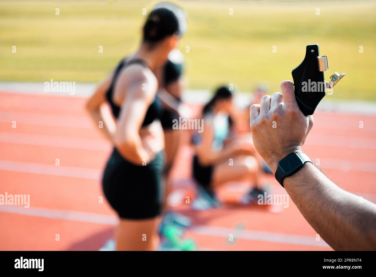 Trying to get them ready. Rearview shot of an unrecognizable man holding a starting gun while a group of sportswomen take up their positions on track. Stock Photo