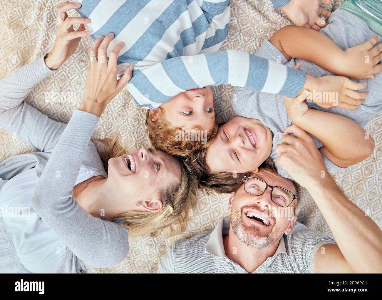 Carefree loving parents from above tickling and teasing their cute little laughing sons. Happy caucasian family of four relaxing and playing together. Cheerful kids spending quality time with mom and dad Stock Photo