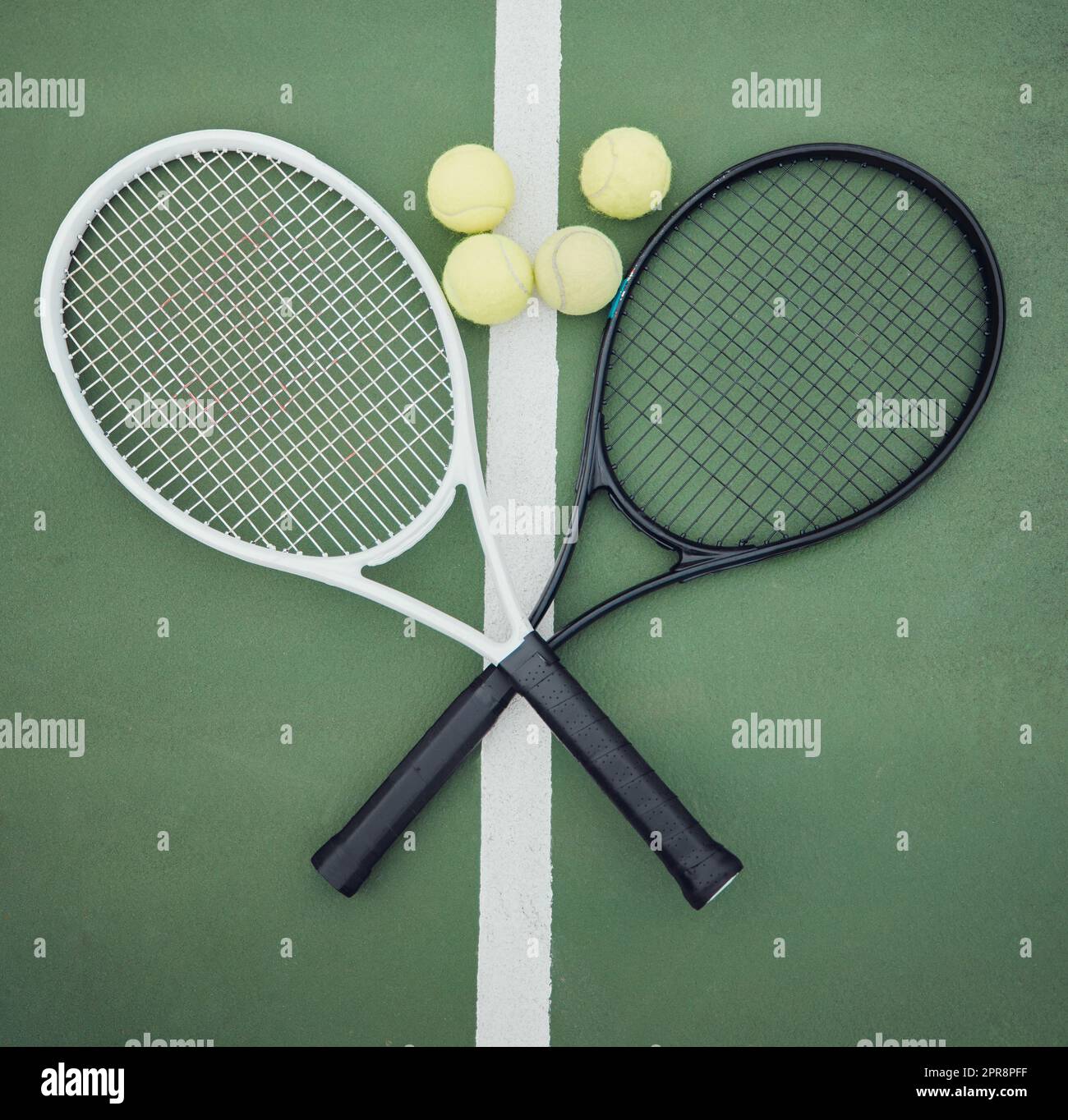 Above view of two tennis rackets and balls on an empty court in a sports club. Aerial view of black and white tennis gear and equipment on asphalt. Ready to play a competitive game versus an opponent Stock Photo