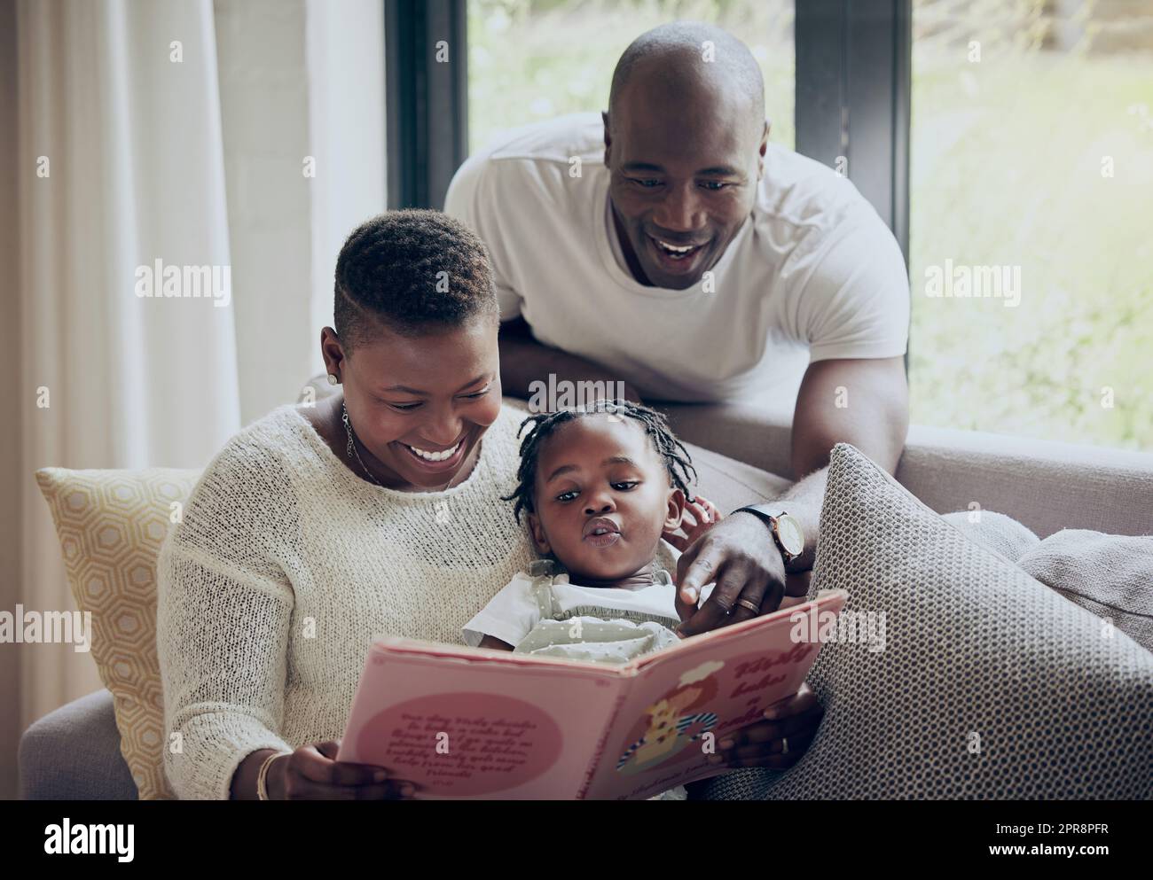 Reading it on her own. a young family reading a book together at home. Stock Photo
