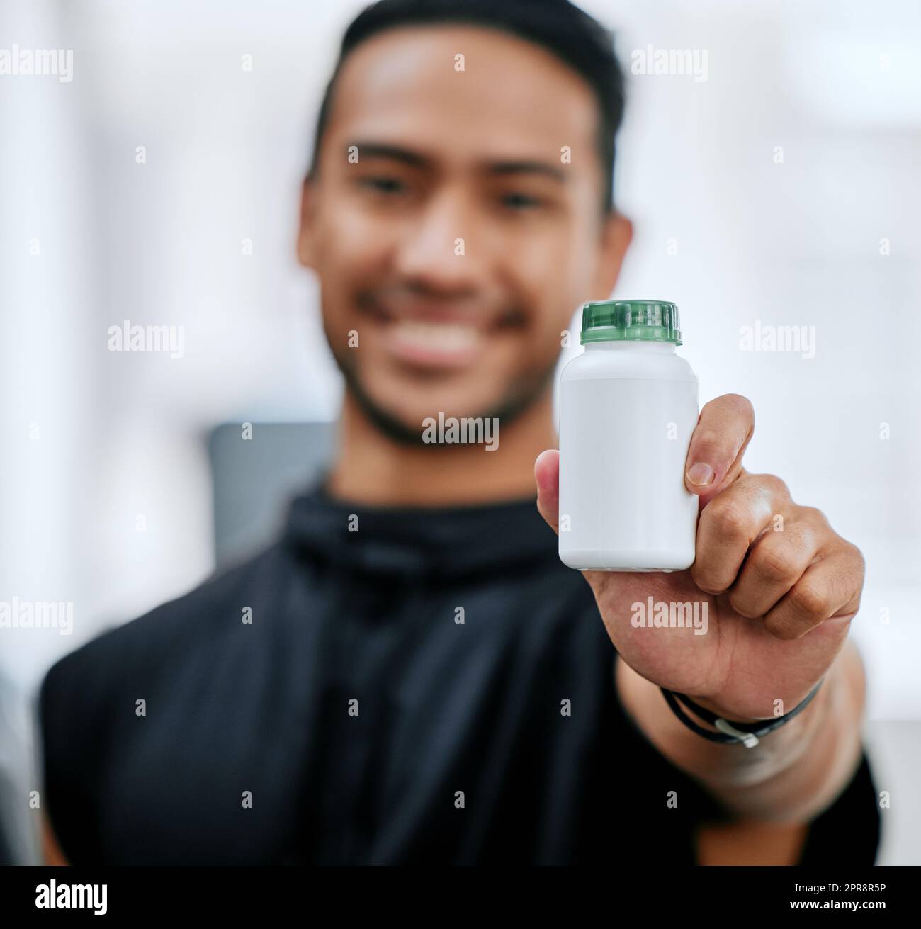 Blur smiling trainer alone in gym while holding and showing bottle of steroid pills. Asian coach with hormone enhancing drugs for workout in exercise health club. Bodybuilder man in fitness centre Stock Photo