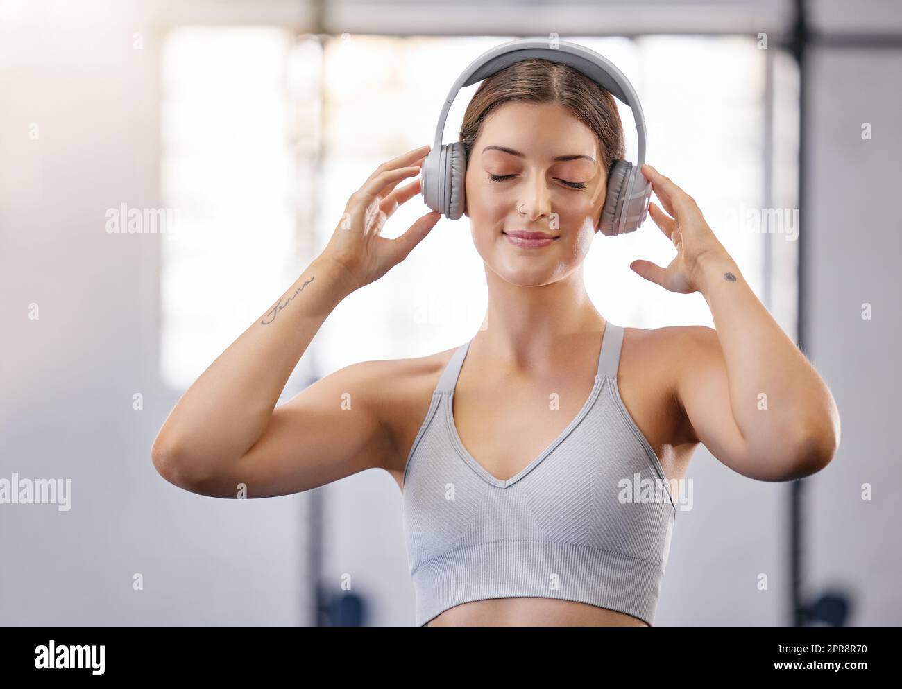 One active young caucasian woman listening to relaxing music with headphones while taking a break from exercise a gym. Female athlete staying motivated with calm music during her workout in a fitness centre Stock Photo