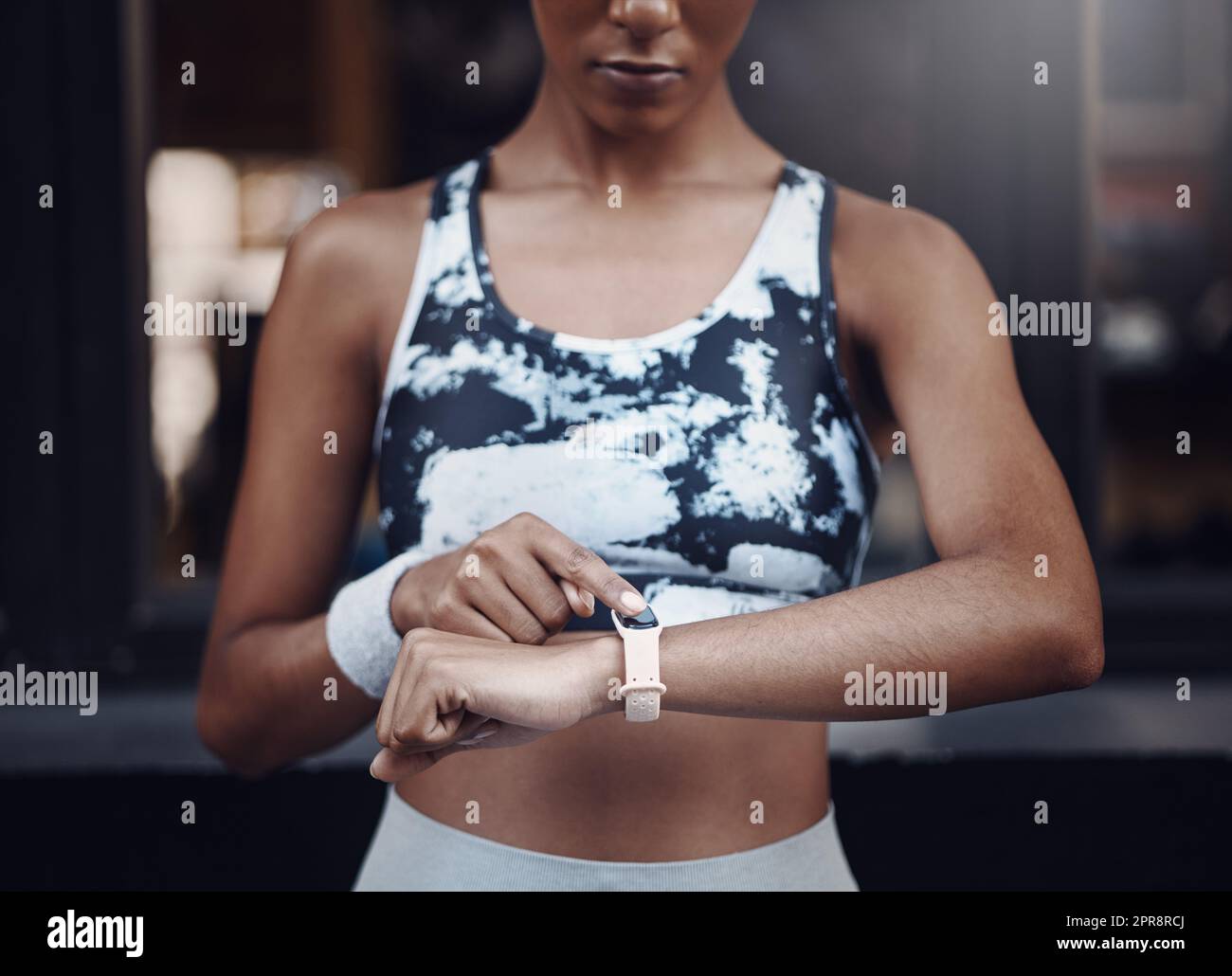 Closeup of one mixed race woman checking time on digital wristwatch with blank display screen while running outdoors. Female athlete wearing fitness tracker on arm to monitor progress, heart rate and calories burned during training exercise in the city Stock Photo