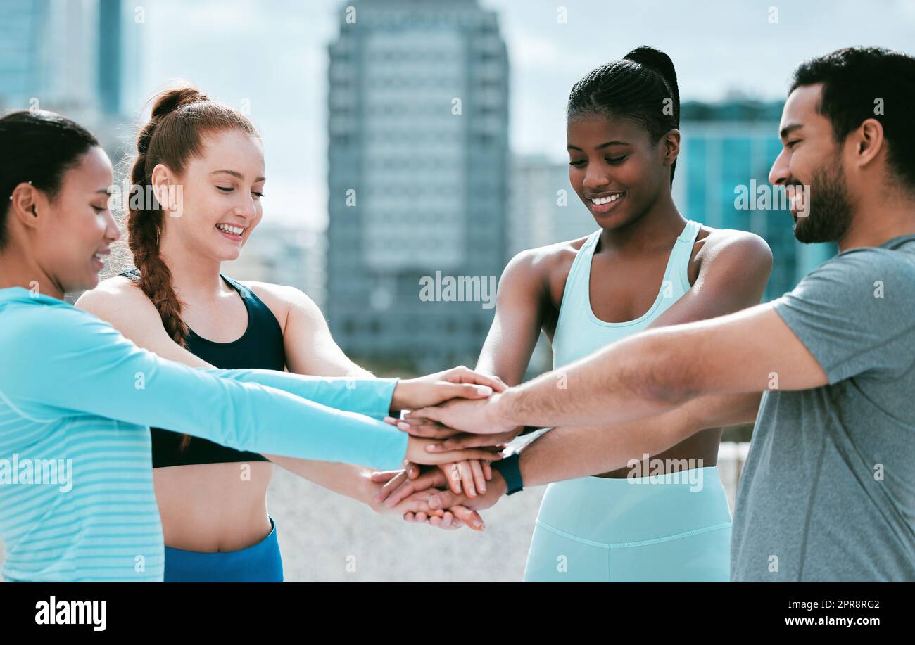 Diverse group of happy sporty people stacking hands together in pile to express unity and support. Motivated athletes huddled in circle for encouraging workout pep talk. Joining for collaboration, team spirit and dedication for training workout in city Stock Photo