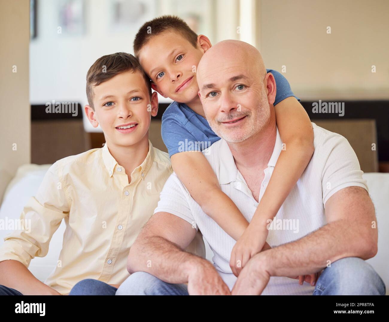 Portrait of happy sons sitting with their father on a comfortable couch at home. Dad bonding with his two kids at home. Mature caucasian man spending time with his children Stock Photo