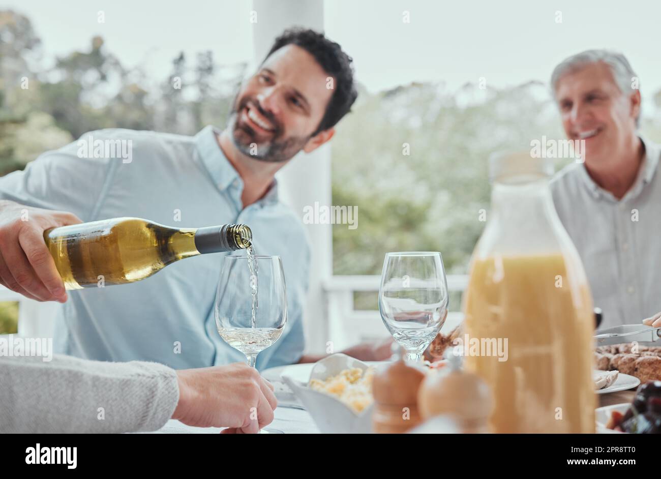 A strong family has well worn seats at the table. a male pouring wine during lunch at home. Stock Photo