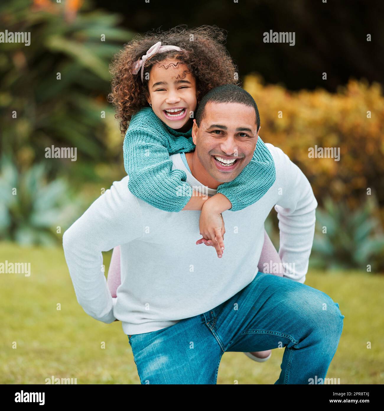 Playing requires a lot of cardio. a man carrying his daughter on his back while playing outside. Stock Photo