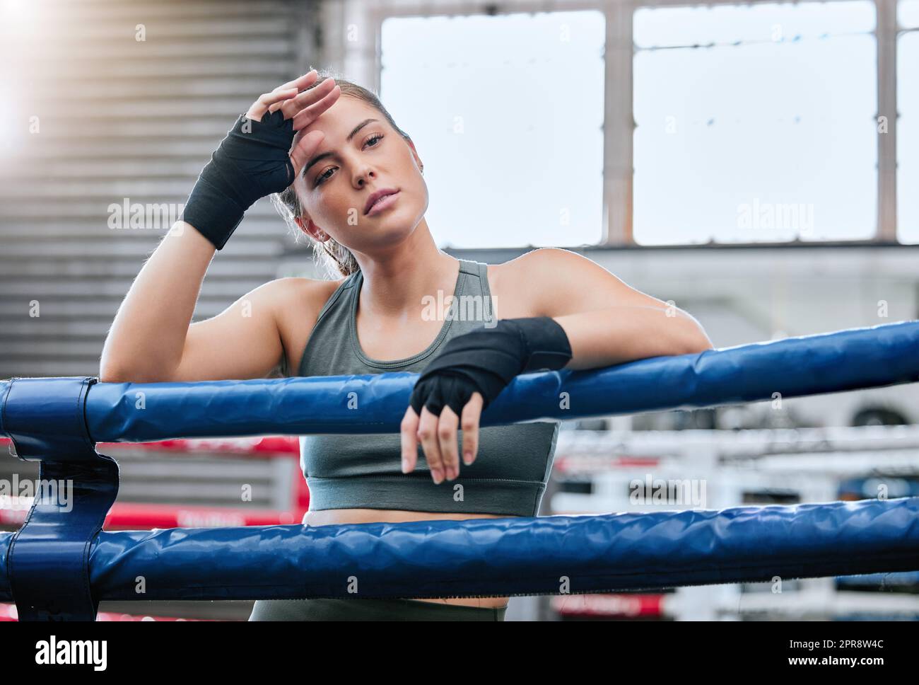 Confident, active and toned female fitness athlete in a boxing ring after a fight, match or sparring session in a gym. A healthy, fit and strong woman ready to exercise, workout and do training Stock Photo