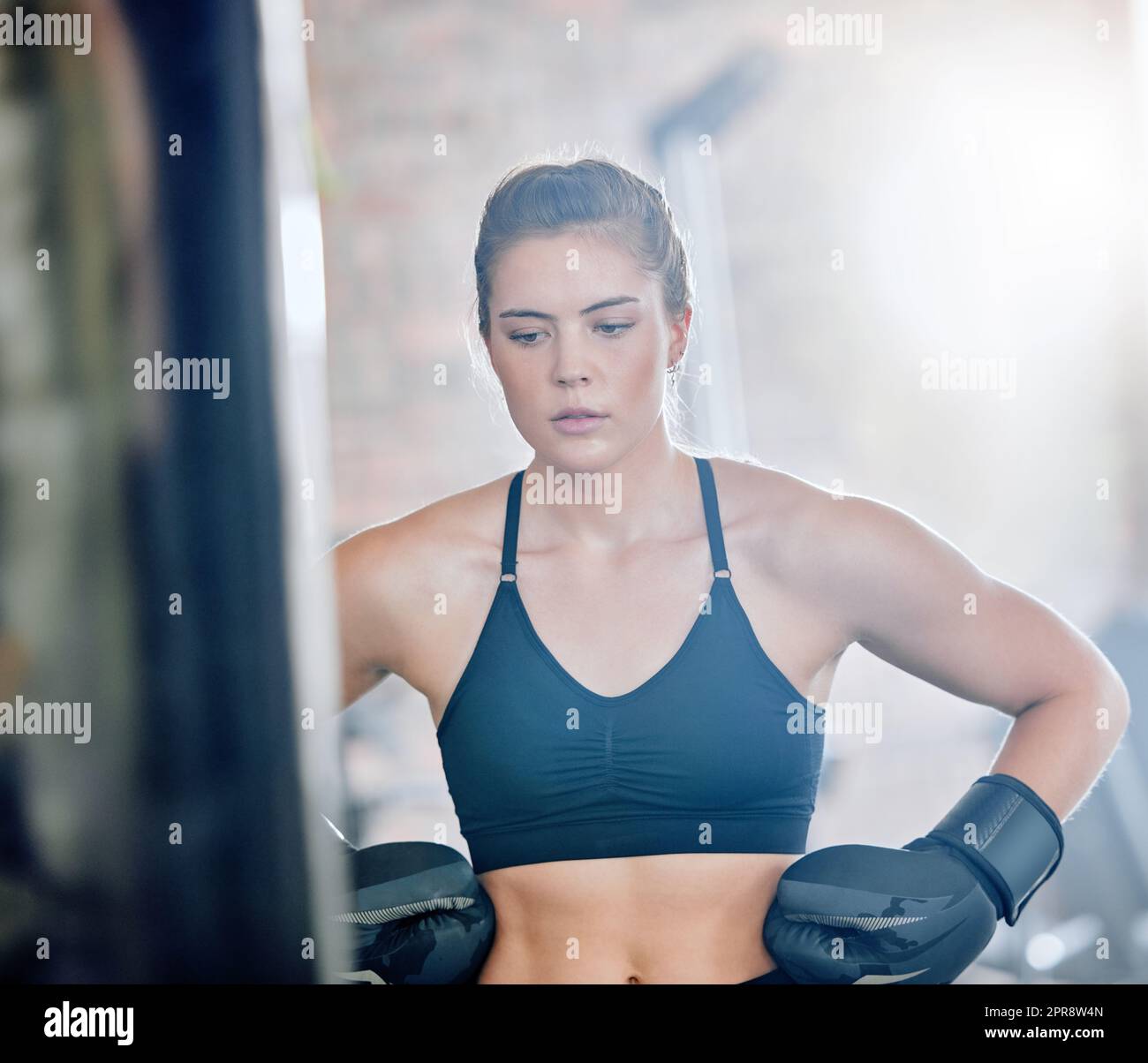 Healthy, fit and active female boxer thinking about a fight, competition or match in the gym or health club. Young woman training, exercising and working out in a fitness studio and looking dedicated Stock Photo