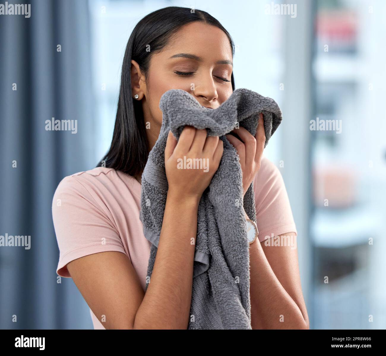 When all else fails, cleaning house is the perfect antidote. a young woman smelling a towel at home. Stock Photo