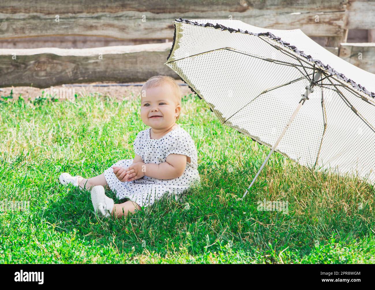 beautiful baby in a polka-dot dress is sitting nea umbrella umbrella Stock Photo