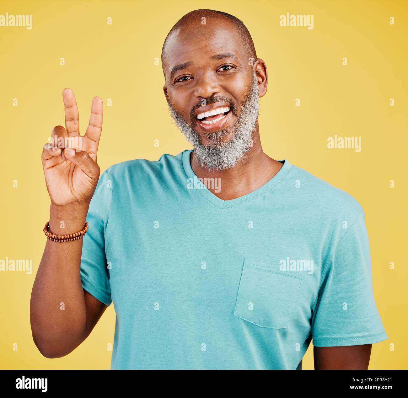 Portrait of a mature friendly african american man looking happy and smiling while making an peace gesture with his hand against a yellow studio background. Expressing that everything is perfect. Showing support Stock Photo