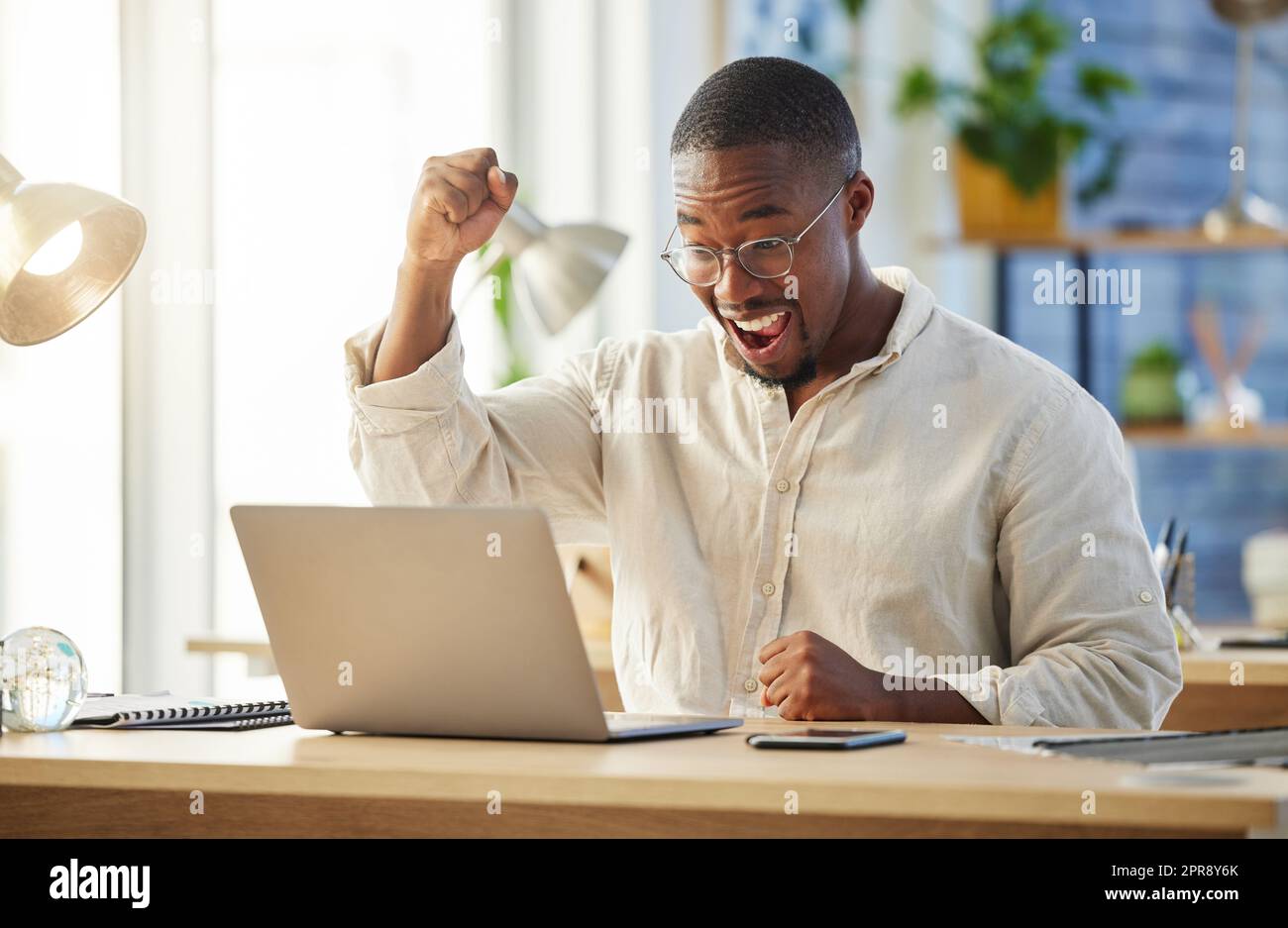 He never thought it would happen. a young businessman cheering in excitement at his desk. Stock Photo