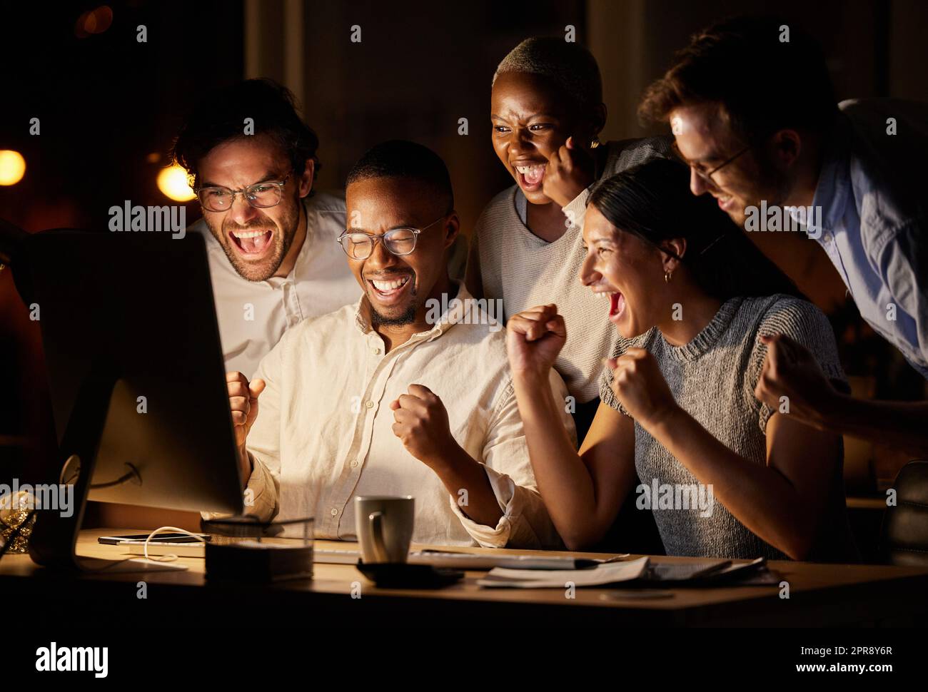 Everything worked out perfectly in the end. a group of businesspeople cheering while working together on a computer in an office at night. Stock Photo