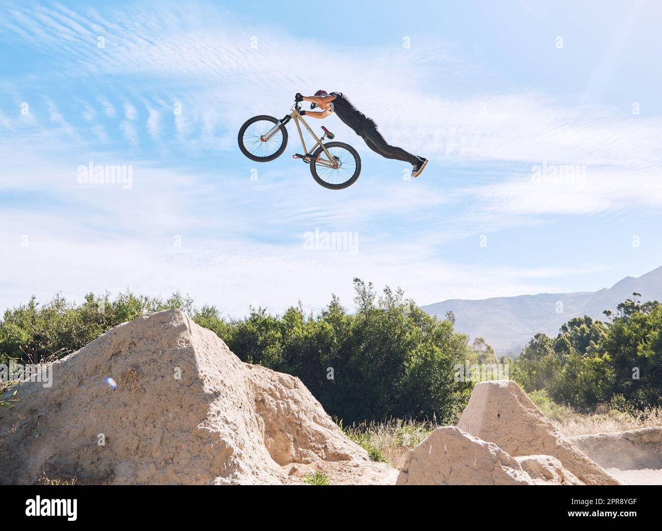 Young man showing his cycling skills while out cycling on a bicycle outside. Adrenaline junkie practicing a dirt jump outdoors. Male wearing a helmet doing extreme sports with a mountain bike Stock Photo