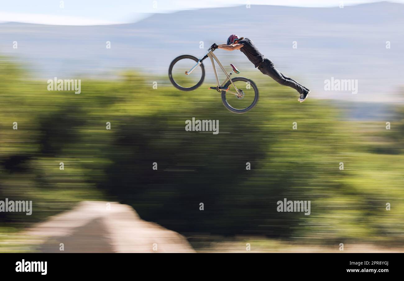 Young man showing his cycling skills while out cycling on a bicycle outside. Adrenaline junkie practicing a dirt jump outdoors. Male wearing a helmet doing extreme sports with a mountain bike Stock Photo