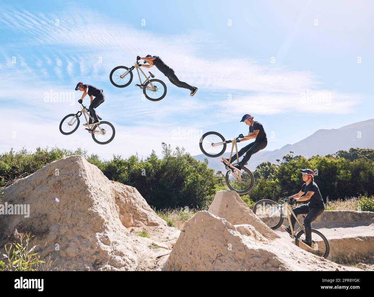 Young man showing his cycling skills while out cycling on a bicycle outside. Adrenaline junkie practicing a dirt jump outdoors. Male wearing a helmet doing extreme sports with a bike. Phases of a jump Stock Photo