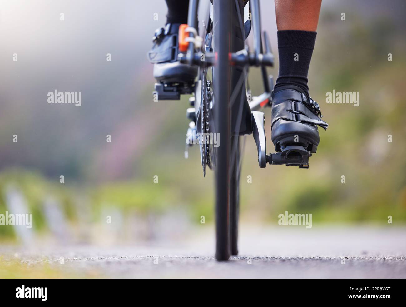 Closeup of one woman cycling outside. Sporty fit female athlete with her feet on bicycle pedals while riding a bike on a road for exercise. Endurance and cardio during a workout and training Stock Photo