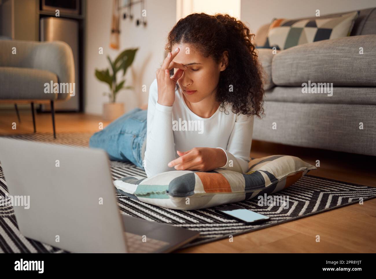 Stressed young woman using her laptop. Young woman experiencing a headache in front of her computer. Laptop issues always happen at home. Woman lying on her floor looking worried Stock Photo