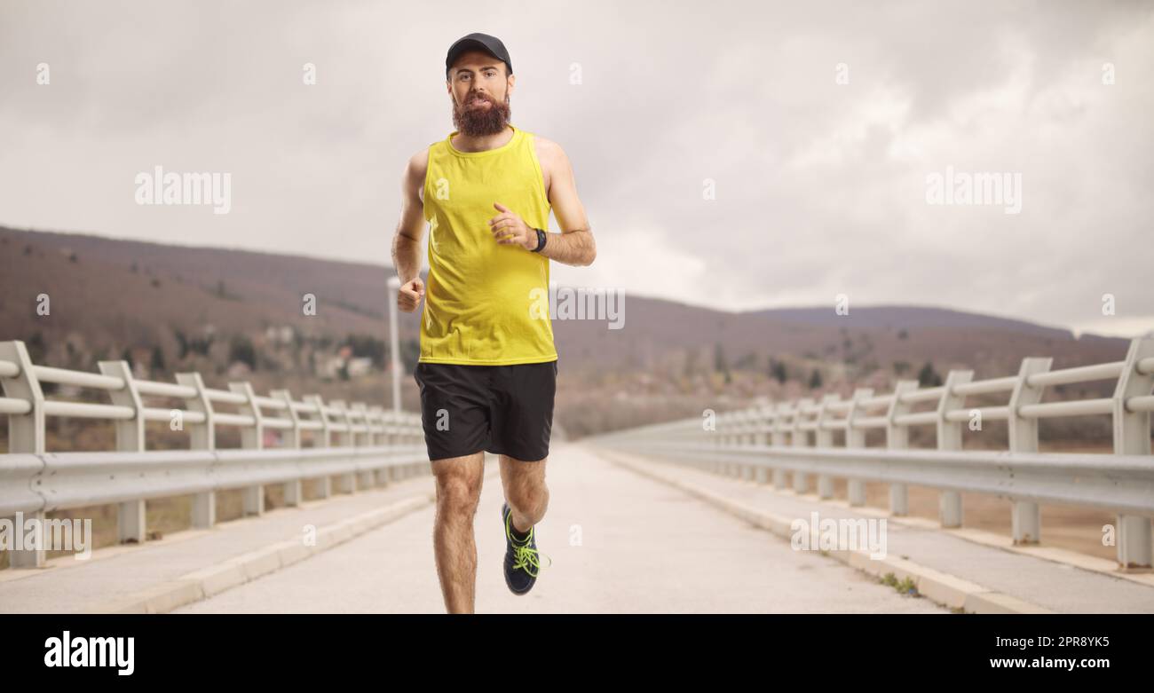 Bearded man with a cap jogging on a bridge Stock Photo